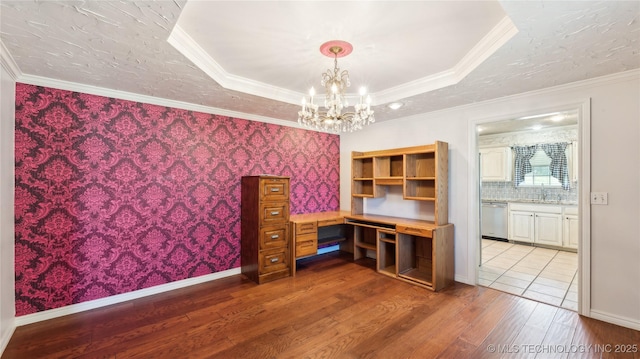 unfurnished office featuring ornamental molding, a tray ceiling, a notable chandelier, and wood finished floors