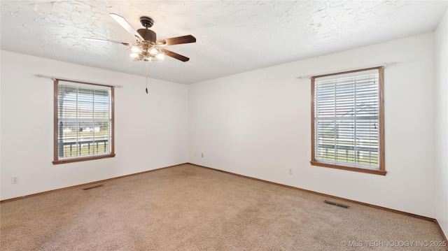 empty room with light carpet, a ceiling fan, visible vents, and a wealth of natural light