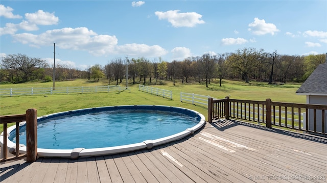 outdoor pool featuring a rural view, a yard, a wooden deck, and fence
