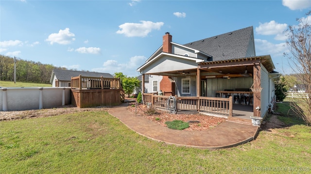 rear view of house with roof with shingles, a deck, a chimney, and a lawn