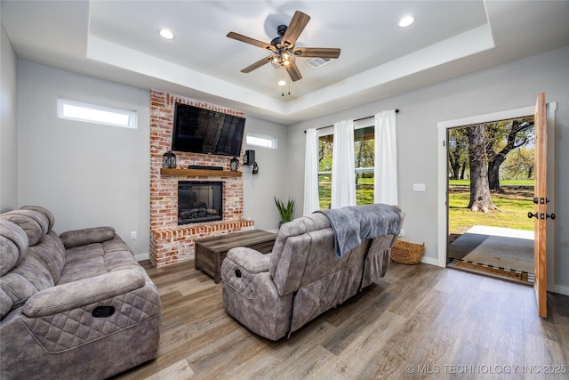 440 W 2nd St, Silo, OK 74701 - living area with a tray ceiling, a healthy amount of sunlight, a brick fireplace, and light wood-style flooring