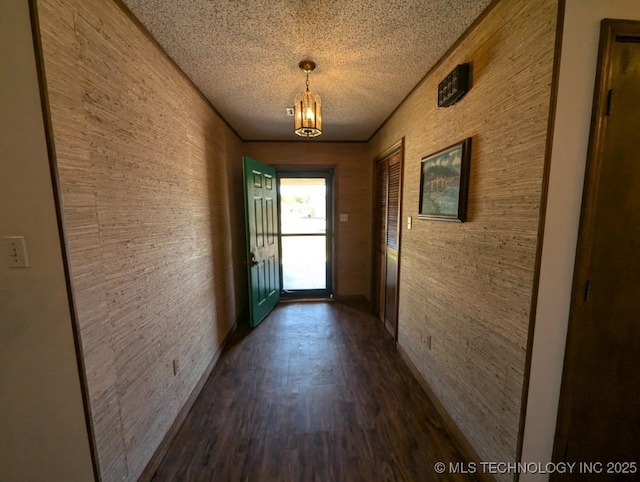 corridor with dark wood-type flooring, a notable chandelier, and a textured ceiling