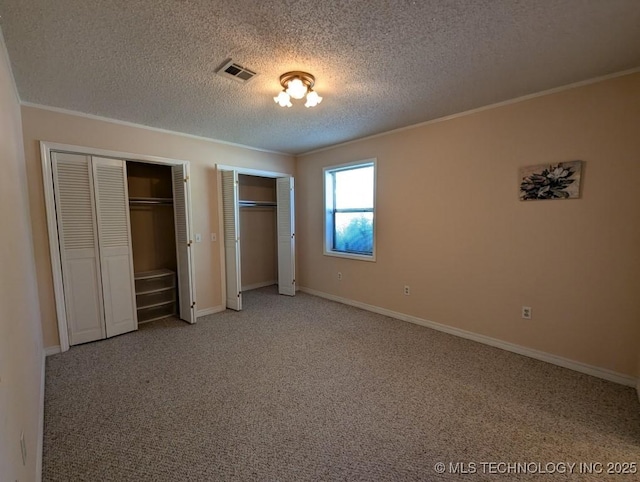 unfurnished bedroom with a textured ceiling, ornamental molding, visible vents, and multiple closets