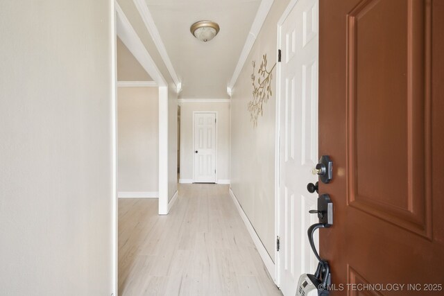 corridor featuring light wood-style flooring, ornamental molding, and baseboards