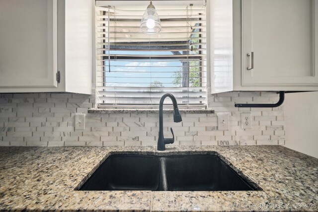 kitchen with white cabinetry, backsplash, light stone counters, and a sink