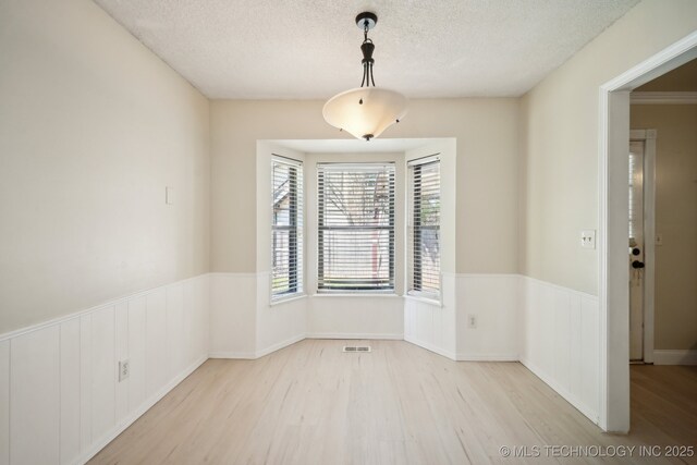 unfurnished dining area featuring visible vents, wood finished floors, wainscoting, and a textured ceiling