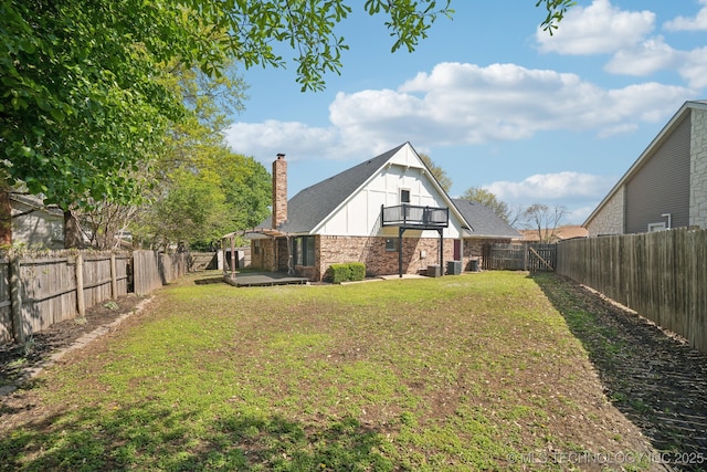 back of house featuring a chimney, board and batten siding, a fenced backyard, a balcony, and a lawn