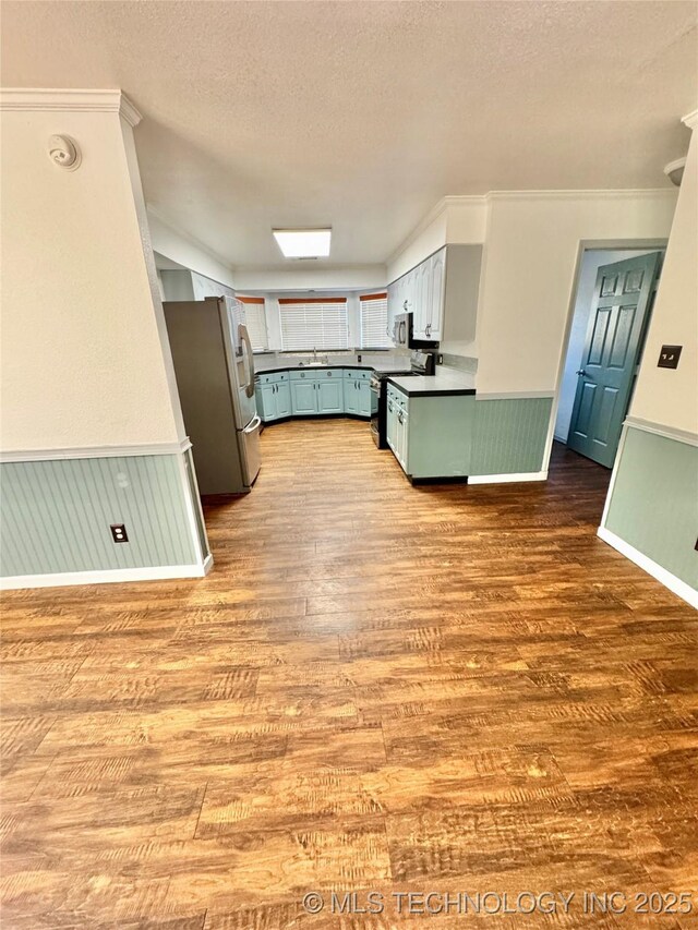 5101 S Spruce Dr, Sand Springs, OK 74063 - kitchen with a sink, appliances with stainless steel finishes, a textured ceiling, wood finished floors, and a wainscoted wall
