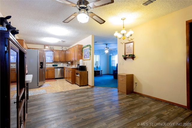 kitchen featuring brown cabinetry, visible vents, light wood-type flooring, ceiling fan with notable chandelier, and stainless steel appliances