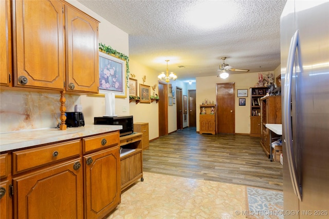 612 W Circle Dr, Broken Bow, OK 74728 - kitchen with freestanding refrigerator, black microwave, brown cabinetry, ceiling fan, and a textured ceiling