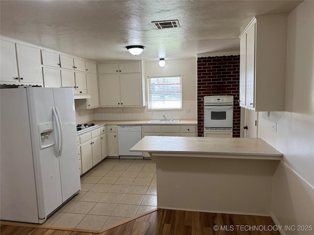 kitchen with a peninsula, a sink, light countertops, and white appliances
