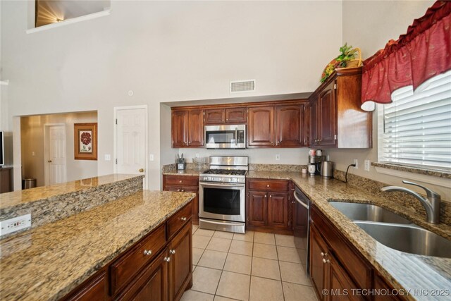4932 W Commercial St, Broken Arrow, OK 74012 - kitchen featuring stainless steel appliances, a towering ceiling, a sink, light tile patterned floors, and light stone countertops