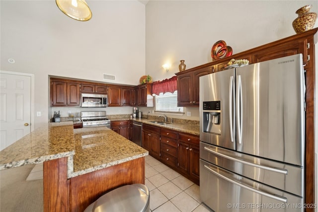 4932 W Commercial St, Broken Arrow, OK 74012 - kitchen featuring appliances with stainless steel finishes, a towering ceiling, a sink, light tile patterned flooring, and light stone countertops