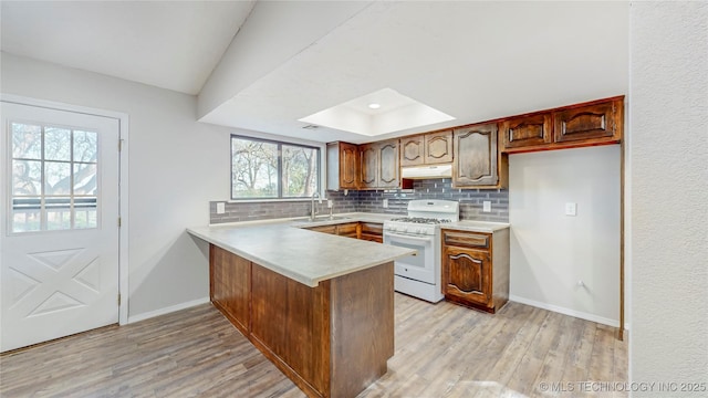 kitchen with a sink, light wood finished floors, white gas range oven, a peninsula, and under cabinet range hood
