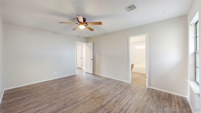 spare room featuring plenty of natural light, wood finished floors, visible vents, a ceiling fan, and baseboards