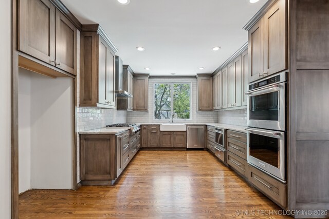 10126 S Granite Ave, Tulsa, OK 74137 - kitchen with stainless steel appliances, light wood-style floors, wall chimney exhaust hood, tasteful backsplash, and recessed lighting