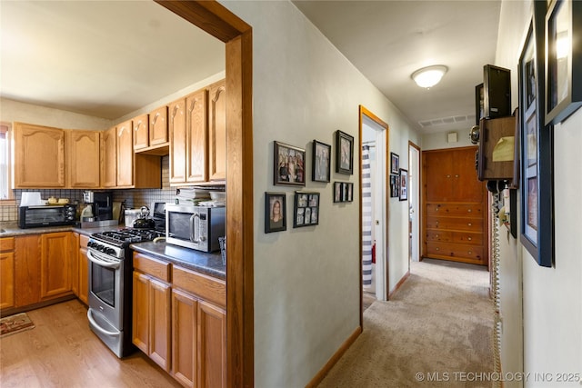 kitchen featuring light wood-style floors, appliances with stainless steel finishes, decorative backsplash, and dark countertops