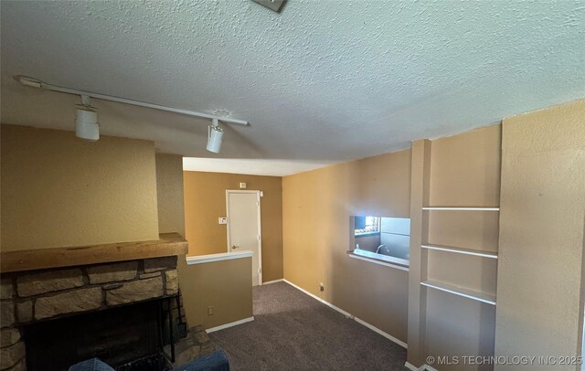 unfurnished living room with a fireplace, track lighting, a textured ceiling, carpet flooring, and baseboards