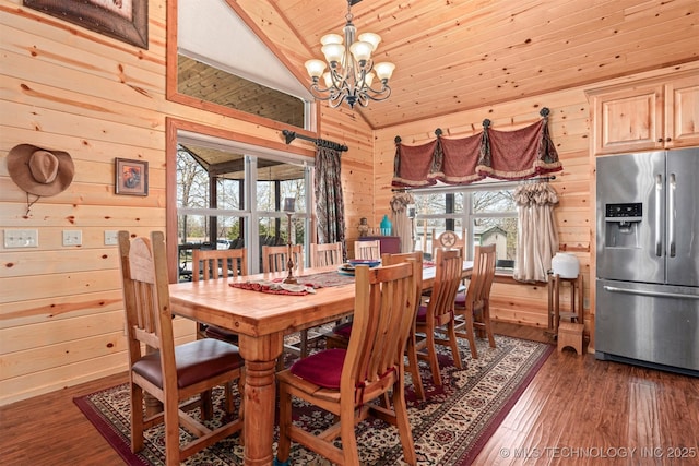 dining room featuring wood walls, a notable chandelier, wood finished floors, and lofted ceiling