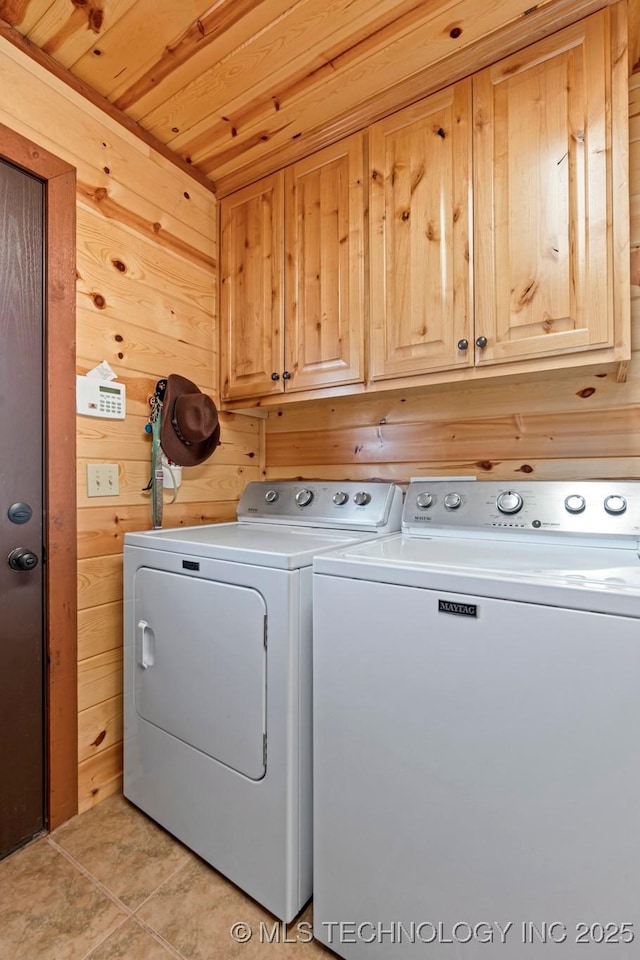 clothes washing area with cabinet space, wood walls, separate washer and dryer, and light tile patterned flooring