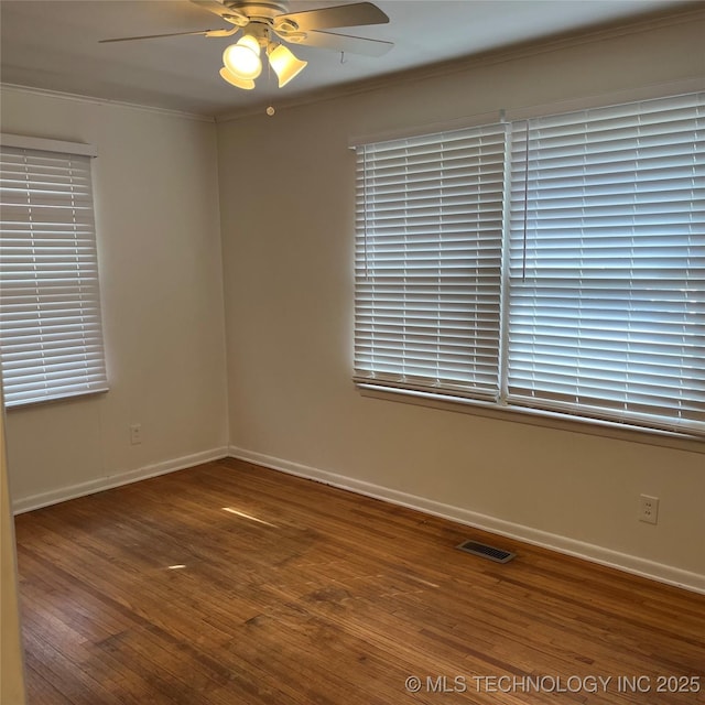 empty room with ceiling fan, ornamental molding, visible vents, wood finished floors, and baseboards