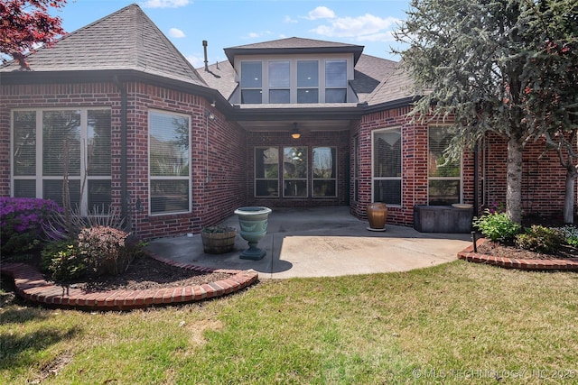 back of house with a lawn, roof with shingles, a patio area, and brick siding