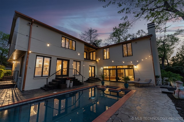 back of house with french doors, a pool with connected hot tub, a chimney, brick siding, and a patio area