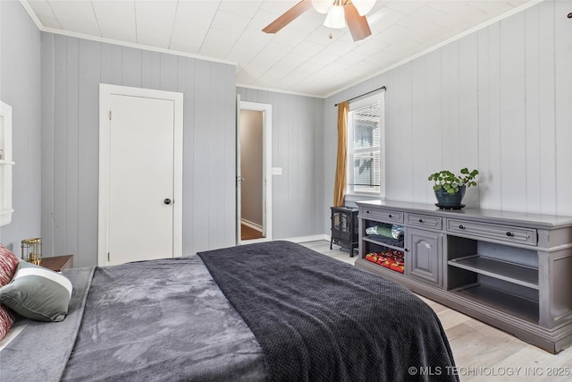 bedroom with wooden walls, ornamental molding, ceiling fan, and light wood-style floors