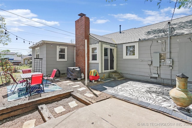 rear view of property with a patio, entry steps, a chimney, and a shingled roof