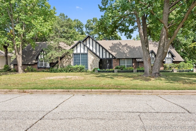 tudor home with a front yard, stone siding, and a shingled roof