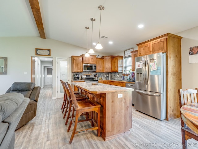 kitchen featuring lofted ceiling with beams, open floor plan, a center island, appliances with stainless steel finishes, and light wood finished floors