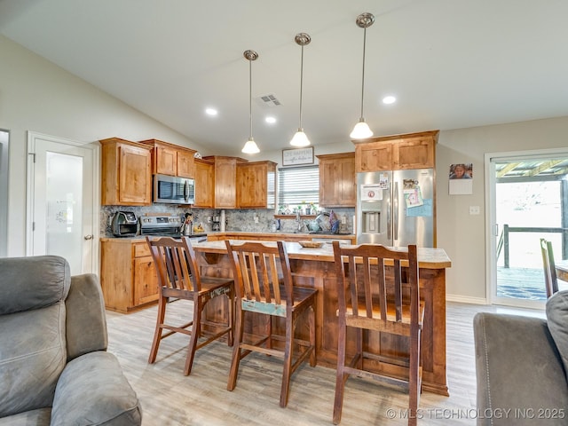 kitchen featuring light wood-style floors, lofted ceiling, stainless steel appliances, open floor plan, and decorative backsplash