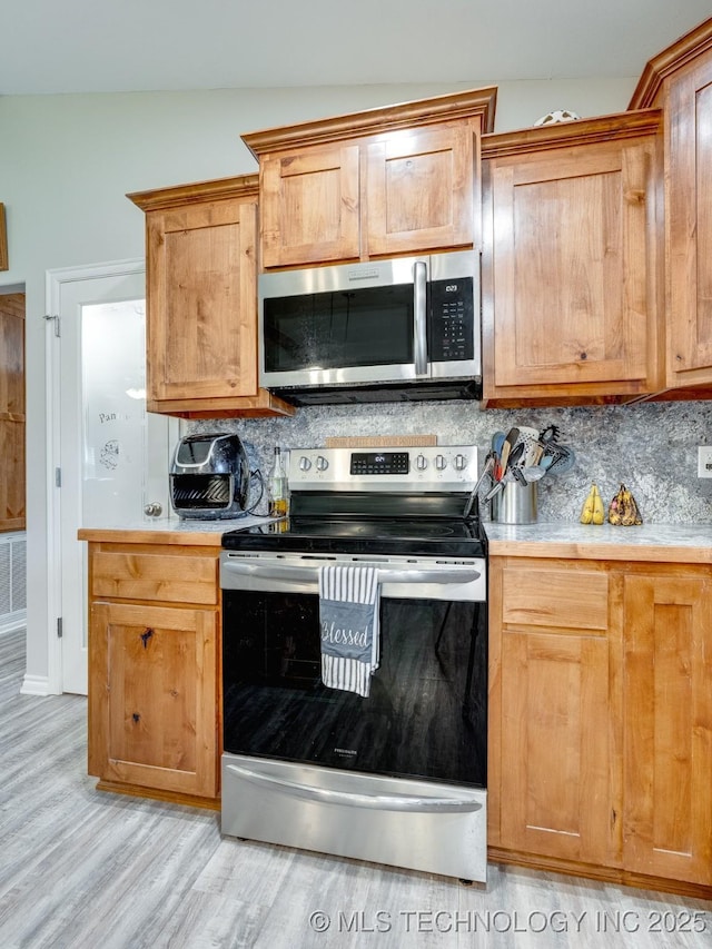 kitchen with tasteful backsplash, light countertops, light wood-type flooring, and stainless steel appliances