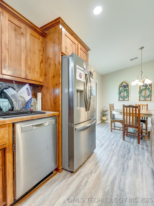 kitchen with visible vents, appliances with stainless steel finishes, a chandelier, brown cabinetry, and light wood finished floors