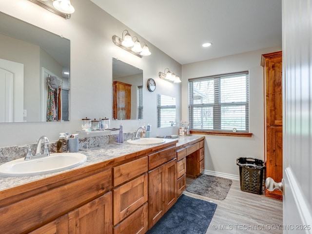 bathroom with a sink, baseboards, double vanity, and wood finished floors