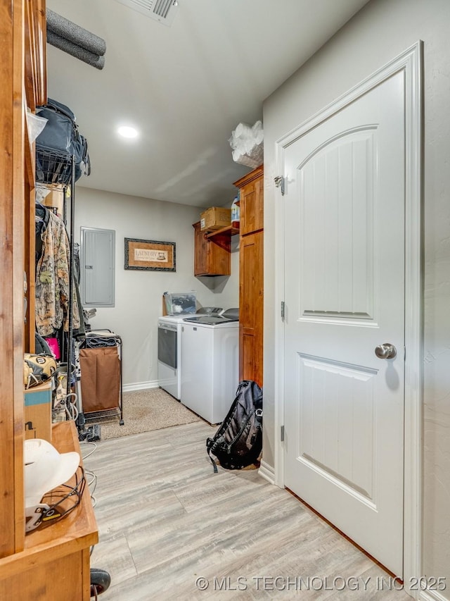 clothes washing area with baseboards, electric panel, cabinet space, light wood finished floors, and washing machine and clothes dryer