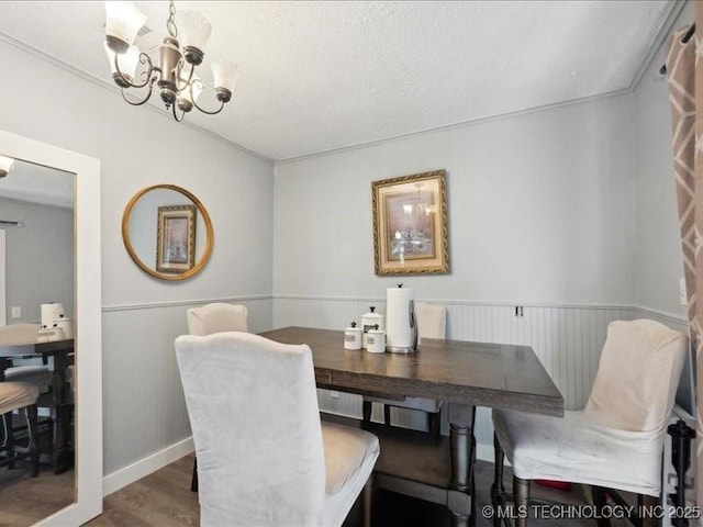 dining space featuring wainscoting, a notable chandelier, wood finished floors, and a textured ceiling