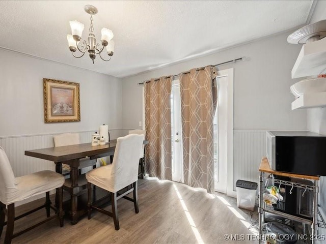 dining space with light wood finished floors, a notable chandelier, and wainscoting