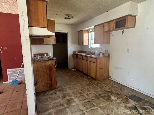 kitchen featuring brown cabinetry, a textured ceiling, visible vents, under cabinet range hood, and a sink