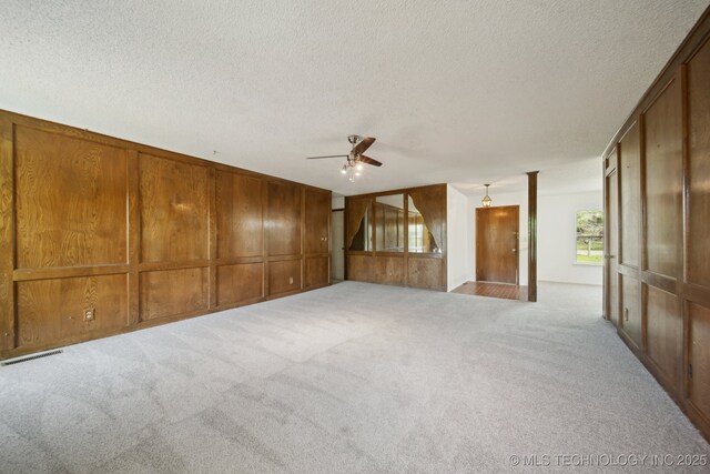 10785 E Dogwood Ct, Claremore, OK 74019 - unfurnished living room featuring carpet flooring, a textured ceiling, a ceiling fan, wood walls, and visible vents