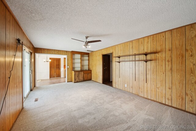 10785 E Dogwood Ct, Claremore, OK 74019 - unfurnished bedroom with wooden walls, a textured ceiling, ceiling fan with notable chandelier, and carpet floors
