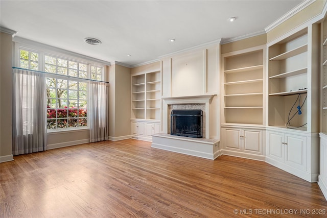 unfurnished living room with built in shelves, ornamental molding, wood finished floors, and a premium fireplace