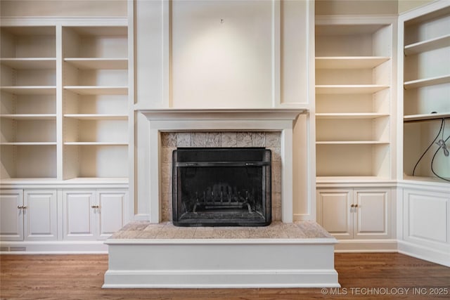 unfurnished living room with visible vents, wood finished floors, built in features, and a fireplace with raised hearth