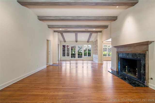 unfurnished living room with lofted ceiling with beams, baseboards, recessed lighting, wood finished floors, and a high end fireplace