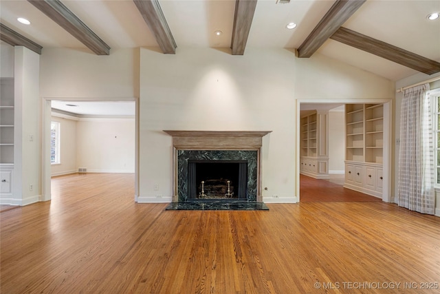 unfurnished living room featuring lofted ceiling with beams, recessed lighting, built in shelves, a premium fireplace, and wood finished floors