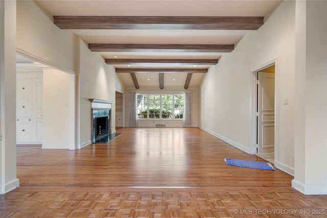 unfurnished living room with light wood finished floors, beam ceiling, visible vents, baseboards, and a premium fireplace