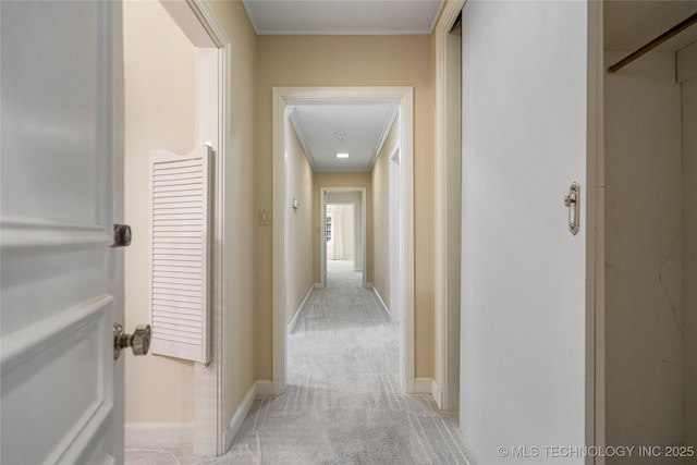 hallway featuring attic access, baseboards, crown molding, and light colored carpet