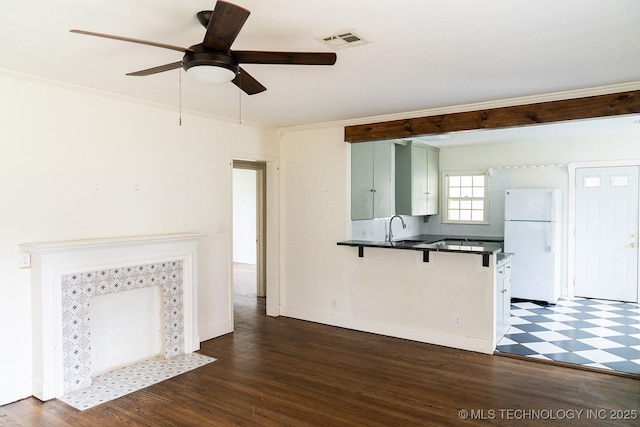 unfurnished living room with visible vents, a sink, ornamental molding, ceiling fan, and dark wood-style flooring