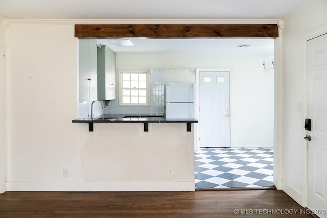 kitchen featuring a breakfast bar, tile patterned floors, a peninsula, freestanding refrigerator, and dark countertops