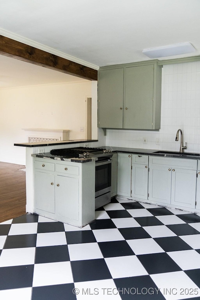 kitchen featuring a sink, dark countertops, stainless steel gas range oven, tile patterned floors, and backsplash